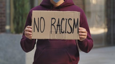 Photo for NO RACISM on cardboard poster in hands of male protester activist. Stop Racism concept, No Racism. Rallies against racism and police brutality. Peaceful life of blacks matters. City street protest - Royalty Free Image
