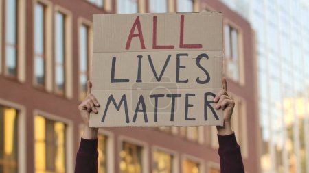 Photo for ALL LIVES MATTER on cardboard poster in hands of male protester activist. Stop Racism concept, No Racism. Rallies against racism and police brutality. Peaceful life of blacks matters. City street - Royalty Free Image