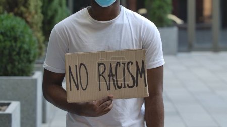 Photo for NO RACISM on cardboard poster in hands of African American male protester activist. Stop Racism concept, No Racism. Rallies against racism and police brutality. Peaceful life of blacks matters. City - Royalty Free Image