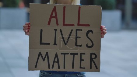 Photo for ALL LIVES MATTER on cardboard poster in hands of female protester activist. Stop Racism concept, No Racism. Rallies against racism and police brutality. Peaceful life of blacks matters. City street - Royalty Free Image
