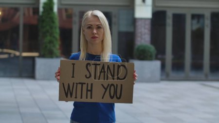 Foto de Mujer joven está de pie con un cartel de cartón I STAND WITH YOU en un lugar público al aire libre. Un activista político protestando en una protesta. No hay racismo sino tolerancia y corrección política en la sociedad. - Imagen libre de derechos