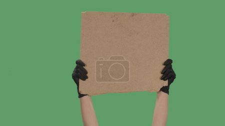Téléchargez les photos : Mains dans les gants noirs ramasser une affiche vierge à partir d'une boîte en carton. Espace vide pour votre slogan, logo ou publicité. Concept de bannière. Isolé un écran vert, clé chromatique - en image libre de droit