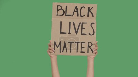 Photo for BLACK LIVES MATTER. Protest text message on sign cardboard. Stop racism. Police violence. Banner design concept. Hands of women raising up poster on green screen, chroma key. Rallies against racism - Royalty Free Image