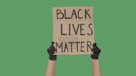 Photo for Female hands in black gloves pick up a poster from a cardboard box that reads BLACK LIVES MATTER. Cardboard banner. Struggle for equality and unity. Isolated on green screen, chroma key. - Royalty Free Image