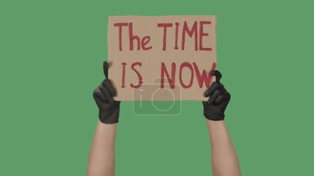 Photo for Hands in black gloves raising up cardboard poster THE TIME IS NOW. Stop Racism concept, No Racism. Rallies against racism and discrimination. Peaceful life of blacks matters. Isolated green screen - Royalty Free Image
