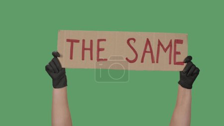 Photo for Sign THE SAME against the background of a green screen, chroma key. Hands in black gloves hold poster from a cardboard box. Black lives matter peaceful protest. Rallies against police brutality and - Royalty Free Image