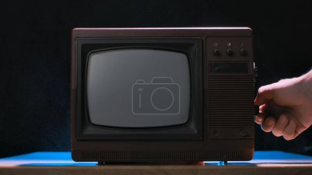Photo for Man turning knob on an old retro TV on black studio background. Vintage analog television. Brown retro media equipment. Retro TV with a turned off screen - Royalty Free Image
