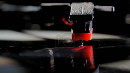 Photo for Macro shot of retro turntable with red tonearm playbacking melody from a record. Stylus of gramophone with needle is touching black vinyl record. Old music player to play music. Concept of nostalgia - Royalty Free Image