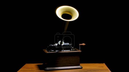 Téléchargez les photos : Classique Edison Phonographe sur une table en bois dans un studio sombre. Machine vintage rétro pour reproduire le son en écoutant de la musique. Instrument de musique antique avec trompette à haut-parleur et rotatif - en image libre de droit