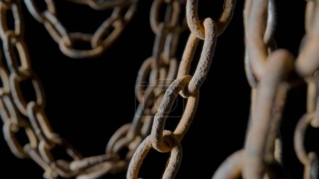 Photo for Rusty metal old chain dangling in dark indoor space. Close up of the links of an aged iron chain covered with corrosion and dust. Rough damaged metal structure. Grunge. Strong uneven metal connections - Royalty Free Image