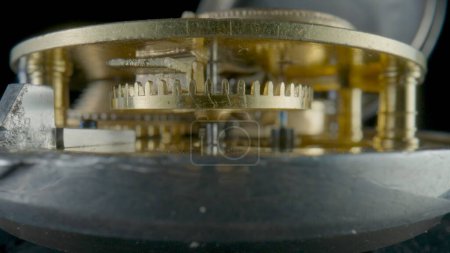 Foto de Vista interior de un reloj de reloj mecánico dorado sobre fondo de estudio aislado negro. Engranajes dorados, engranajes, rueda con dientes. Reloj desmontado con rueda dentada y mecanismo interno. Primer plano de - Imagen libre de derechos