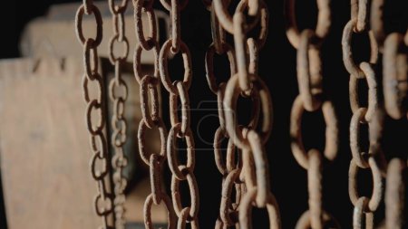 Foto de Rusty metal old chain dangling in dark indoor space. Close up of the links of an aged iron chain covered with corrosion and dust. Rough damaged metal structure. Grunge. Strong uneven metal connections - Imagen libre de derechos