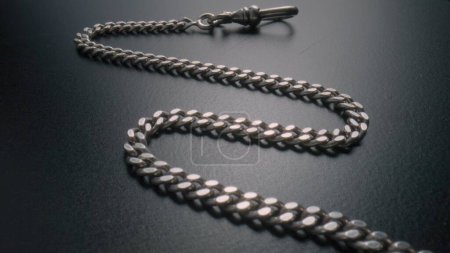 Foto de The silver chain lies on the gray surface of the table. Old retro bracelet with silvery links. Metal vintage pocket watch chain. Old bangle, necklace. Jewellery, bijouterie, expensive luxury jewelry - Imagen libre de derechos