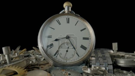 Foto de Antiguo reloj de bolsillo de plata en una pila de engranajes, ruedas dentadas, ruedas dentadas y una pulsera de reloj de metal sobre fondo negro. Piezas desmontadas relojería de relojes antiguos en taller, reparación. Reloj roto - Imagen libre de derechos