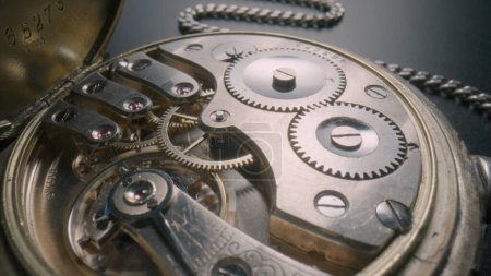 Foto de Mecanismo de trabajo interno de un reloj de bolsillo antiguo sobre un fondo gris. Reverso de un reloj de bolsillo con un reloj abierto y cadena de plata. Tornillos, muelles, engranajes y ruedas dentadas de un reloj antiguo - Imagen libre de derechos