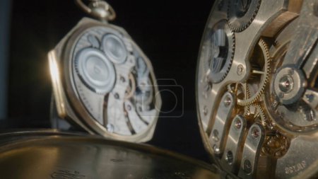 Foto de Dos antiguos relojes de bolsillo de oro con mecanismo de relojería sobre fondo de estudio negro aislado. Cierra los engranajes dentro del viejo reloj de bolsillo mecánico. Mecanismo de reloj con muelle, engranajes, engranajes y ruedas dentadas - Imagen libre de derechos