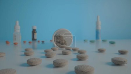 Téléchargez les photos : Round gray pills scattered from bottle on table on blue background. Gray tablets against the background of various medical bottles with medicines. Vitamins, antibiotics or painkillers. Concept of - en image libre de droit