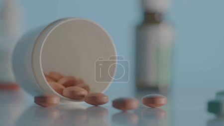 Photo for Round brown pills scattered from bottle on table on blue background. Brown tablets against the background of various medical bottles with medicines. Close up of vitamins, antibiotics or painkillers - Royalty Free Image