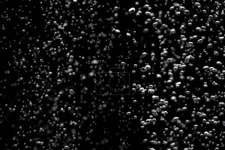 Foto de Burbujas de aire brillantes bajo el agua que se elevan desde el fondo e iluminadas por rayos de luz. Corriente de burbujas de oxígeno sobre un fondo negro aislado. Cierre de un líquido burbujeante durante la aireación del agua en un - Imagen libre de derechos