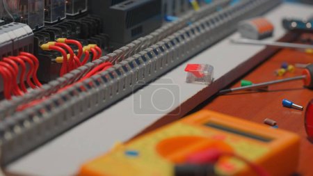 Foto de Caja de plástico gris con bobinas electromagnéticas. Alambres rojos con orejetas amarillas, multímetro y destornillador sobre una mesa en un taller eléctrico - Imagen libre de derechos