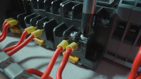 Foto de Panel eléctrico de plástico gris con muchos alambres rojos y polainas de casquillo amarillo. El primer plano del destornillador es sujetar el alambre con el tornillo. Interruptor eléctrico de alto voltaje en un taller eléctrico - Imagen libre de derechos