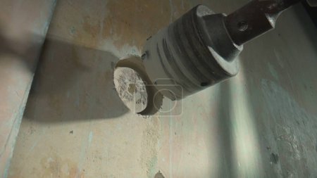 Foto de Drilling a round hole for socket on a gray concrete wall. Round nozzle cup on an electric drill or perforator. Concept of repair, construction, reconstruction. Close up - Imagen libre de derechos