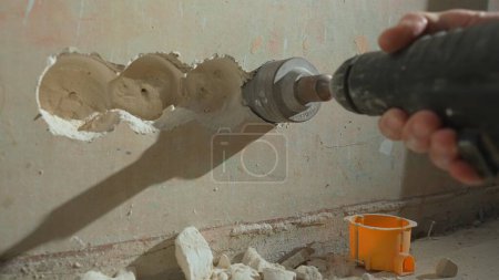Foto de Man drilling round hole in concrete wall for socket. Builder drills hole with electric drill or perforator. Concept of repair, construction, reconstruction. Hands and power tool close up - Imagen libre de derechos