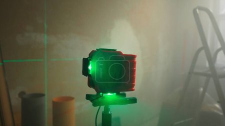 Foto de Green beam of red laser roulette is displayed on brown wall. Lines are intersecting and indicating the location of the mark. Level measurement with a laser ruler. Room under renovation with ladder and - Imagen libre de derechos