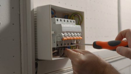 Foto de Electrician assembles electrical panel. Close up of a man hands tightening screw with a screwdriver in a switchboard high voltage electrical switches. Switch box with automatic fuses, wires, switches - Imagen libre de derechos
