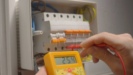 Photo for Work under voltage, electrician is checking serviceability of equipment, measuring voltage by yellow multimeter. Close up of a mans hands testing white switch box check voltage switchboard. Search for - Royalty Free Image