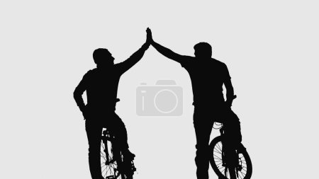 Foto de Vista trasera sobre silueta negra de dos ciclistas saludándose mientras están sentados en bicicletas sobre fondo blanco. Los hombres golpean con las manos, aplaudiendo sus palmas en gesto de saludo. Activo - Imagen libre de derechos