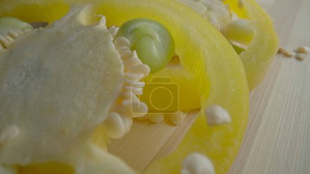 Foto de Sliced rings of fresh raw yellow bell peppers on wooden board. Sweet pepper slices with seeds and juicy pulp in macro shot. Background of ripe vegetables for restaurant. Ripe juicy pepper for salad - Imagen libre de derechos