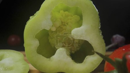 Foto de Cut yellow pepper. Juicy pulp of sweet pepper with seeds inside and moisture droplets in a macro shot. Yellow bell peppers, ripe tomatos and garlic lying on wooden board on isolated black studio - Imagen libre de derechos