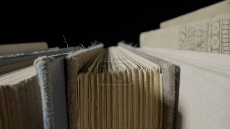 Photo for Macro shot of yellowed paper pages of books in shabby covers on a black background. A row of old textbooks, ancient literature. Literary archive of publications in the library. Learning, knowledge - Royalty Free Image