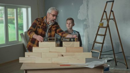 Photo for Grandpa shows his grandson how the water level installed on a brick wall works. An elderly man demonstrates the work of level and a teenager carefully looks and studies. The concept of family, joint - Royalty Free Image