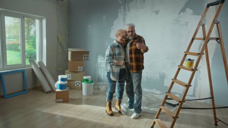 Photo for Elderly man and woman are talking on a video call using their mobile phone. Aged couple communicates with someone and showing repairs in the apartment, ladder, cardboard boxes, a window and wallpaper - Royalty Free Image