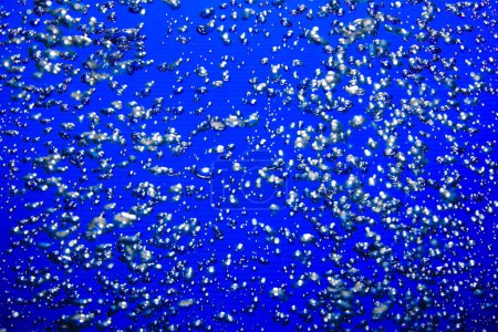 Téléchargez les photos : A lot of shiny air bubbles of different sizes underwater on a blue background. Close up of light lit oxygen bubbles flow upwards. Aeration or filtration of liquid. Fizzy stream of air bubbles - en image libre de droit