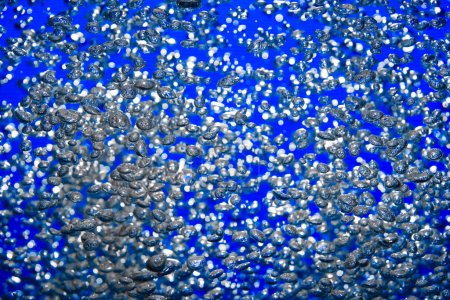 Foto de Una gran cantidad de burbujas de aire brillantes de diferentes tamaños bajo el agua sobre un fondo azul. El primer plano de burbujas de oxígeno iluminadas por la luz fluye hacia arriba. Aireación o filtración de líquido. Fizzy corriente de burbujas de aire - Imagen libre de derechos
