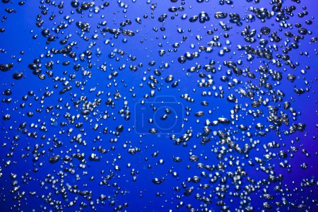 Téléchargez les photos : A lot of shiny air bubbles of different sizes underwater on a blue background. Close up of light lit oxygen bubbles flow upwards. Aeration or filtration of liquid. Fizzy stream of air bubbles - en image libre de droit