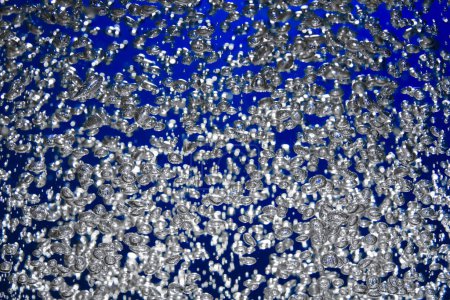 Téléchargez les photos : Beaucoup de bulles d'air brillantes de différentes tailles sous l'eau sur un fond bleu. Gros plan des bulles d'oxygène éclairées par la lumière coulent vers le haut. Aération ou filtration du liquide. Flux vertigineux de bulles d'air - en image libre de droit