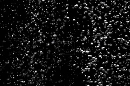 Foto de A lot of shiny air bubbles of different sizes underwater on a black isolated background. Close up of light lit oxygen bubbles flow upwards. Aeration or filtration of liquid. Fizzy flow of air bubbles - Imagen libre de derechos