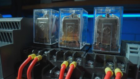 Foto de Relay with electromagnetic coils of direct and alternating current, red wires with yellow bushing ferrules. Automatic electrical switch in an electrical workshop. Close up of electrical parts of - Imagen libre de derechos