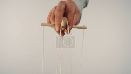 Téléchargez les photos : The puppeteers hand controls the puppet with a wooden manipulator and strings. The marionettist controls and pulls the strings on a white isolated background. Concept of dependence, dominance - en image libre de droit