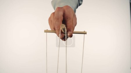 Téléchargez les photos : The puppeteers hand controls the puppet with a wooden manipulator and strings. The marionettist controls and pulls the strings on a white isolated background. Concept of dependence, dominance - en image libre de droit