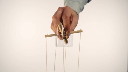 Téléchargez les photos : The hand of a man in a gray shirt controls a puppet using a wooden manipulator and strings. Hand handling at puppet by pulling strings to make the character move. Concept of mind manipulation, boss - en image libre de droit
