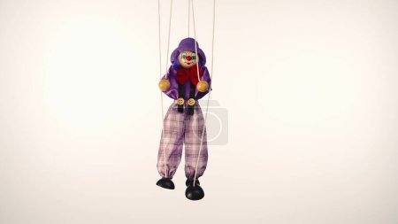 Foto de Payaso marioneta colgando de cuerdas. Muñeca de trapo con traje y sombrero púrpura, con lazo rojo, nariz y maquillaje. Muñeca suave arlequín funster sobre un fondo de estudio blanco. El concepto de unas vacaciones para niños - Imagen libre de derechos