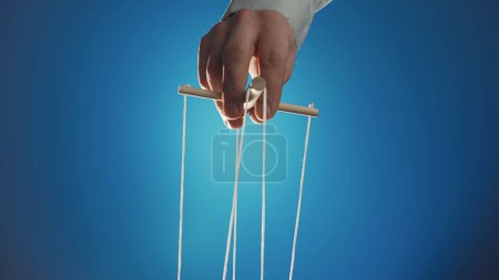 Téléchargez les photos : The puppeteers hand controls the puppet with a wooden manipulator and strings. The marionettist controls and pulls the strings on a blue isolated background. Concept of dependence, dominance - en image libre de droit