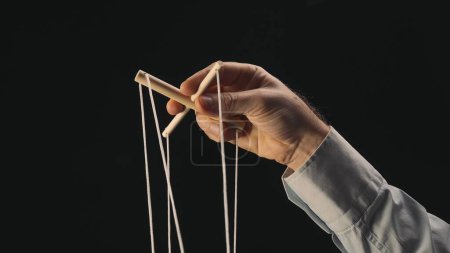 Photo for The puppeteers hand controls the puppet with a wooden manipulator and strings. The marionettist controls and pulls the strings on a black background. The concept of dependence, dominance, managing - Royalty Free Image
