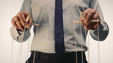 A businessman in a gray shirt and black tie controls a puppet with a wooden manipulator and strings. The puppeteer manipulates the puppet by pulling the ropes with both hands on a white background