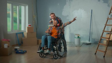 Foto de Un hombre blanco llevando a una mujer afroamericana en silla de ruedas a la habitación. Una pareja joven con auriculares grandes disfruta de la música, canta usando un rodillo como micrófono. El concepto de renovación en el - Imagen libre de derechos